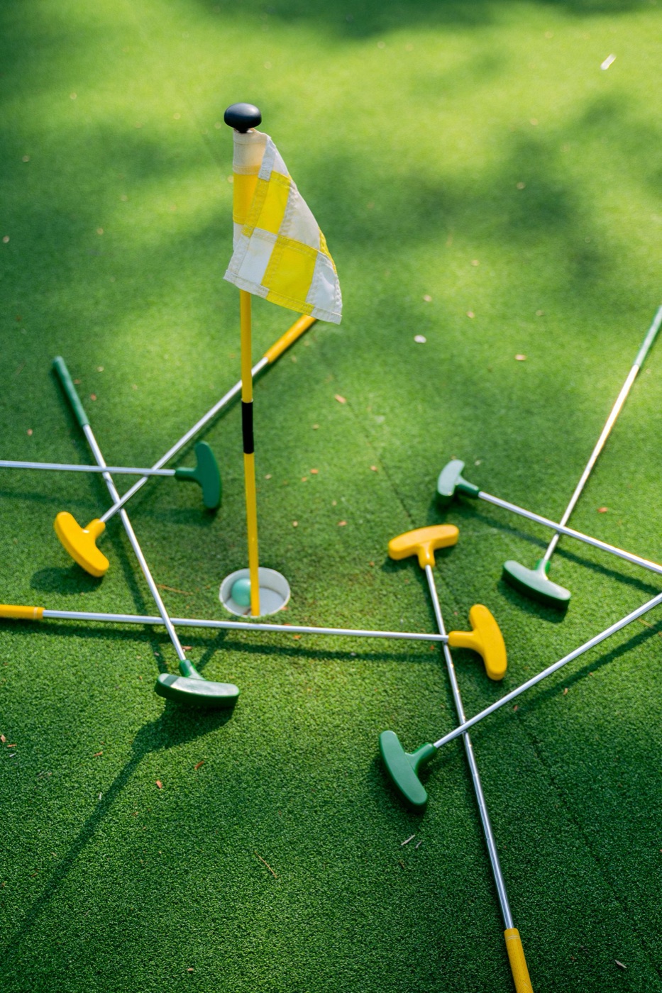 Colorful mini-golf putters around a hole on green turf